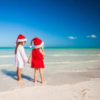 bak- se av liten söt flickor i jul hattar på de exotisk strand foto