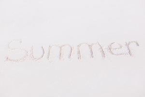ord sommar handskriven på sandig strand med mjuk hav Vinka på bakgrund foto