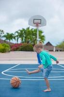 liten flicka med basketboll på domstol på tropisk tillflykt foto