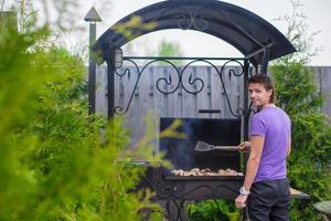 ung man frites biffar på de grill utomhus- i hans gård foto