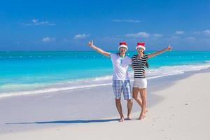 ung Lycklig par i röd santa hattar på tropisk strand foto