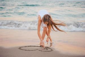 söt tonåring flicka med lång hår ha roligt på de strand och teckning på de sand foto