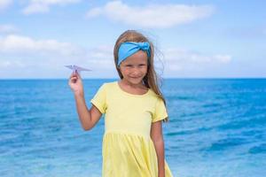 Lycklig liten flicka med papper flygplan i händer på vit sandig strand foto