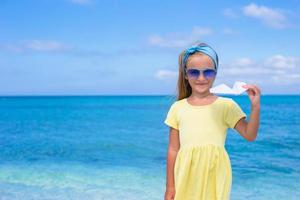 Lycklig liten flicka med papper flygplan på vit sandig strand foto