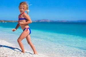 liten flicka har roligt njuter semester på tropisk strand med vit sand och turkos hav vatten foto