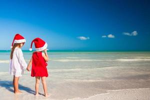 liten förtjusande flickor i santa hattar under strand semester foto