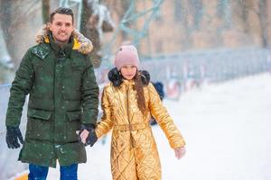 ung pappa och förtjusande liten flicka ha roligt på skridskoåkning rink utomhus foto