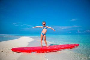 liten bedårande flicka tränar surfposition på stranden foto