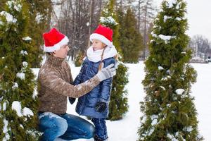 Lycklig familj i santa hattar med jul träd utomhus foto
