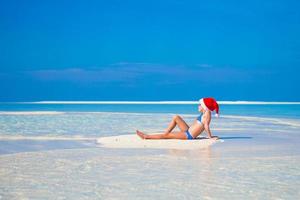 liten söt flicka i santa hatt på vit strand under semester foto