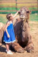 liten flicka med kameler i de Zoo på värma och solig sommar dag. aktiva familj fritid. foto