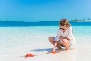 förtjusande liten flicka med sjöstjärna på vit strand foto