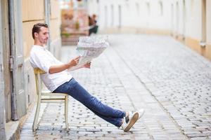 man turist med en stad Karta och ryggsäck i Europa gata. caucasian pojke ser med Karta av europeisk stad. foto