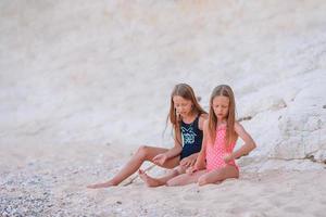 två liten Lycklig flickor ha en massa av roligt på tropisk strand spelar tillsammans foto