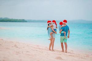 Lycklig familj i röd santa hattar på en tropisk strand fira jul semester foto
