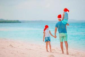 Lycklig familj i röd santa hattar på en tropisk strand fira jul semester foto