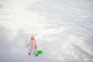 förtjusande liten Lycklig flicka sledding i vinter- snöig dag. foto