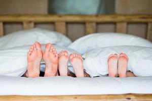 familj med två barn om i säng med deras fötter framåt- foto