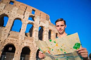 ung turist med Karta i främre av colosseum. ung man sökande de attraktion bakgrund de känd område i rom, Italien foto