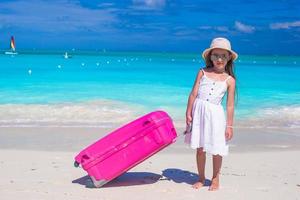 liten förtjusande flicka med stor bagage i händer på tropisk strand foto