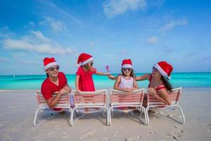 Lycklig familj i jul hattar har roligt på vit strand foto