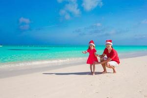liten flicka och lycklig pappa i santa hatt på den exotiska stranden foto