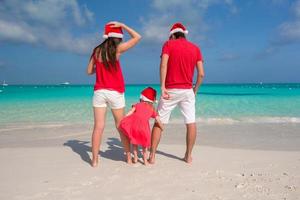 Lycklig familj av tre i jul hattar under tropisk semester foto