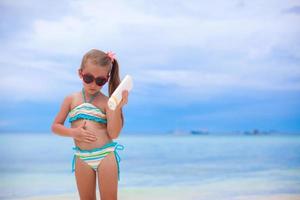 liten förtjusande flicka i baddräkt innehar solbränna lotion flaska foto