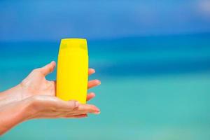 kvinnliga händer med suncream flaska bakgrund blå havet foto