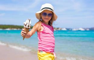 liten förtjusande flicka med is grädde på tropisk strand foto