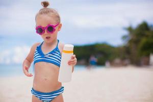 liten förtjusande flicka i baddräkt med solbränna lotion flaska foto