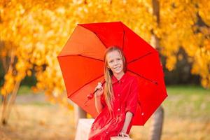 Lycklig barn flicka skrattar under röd paraply foto