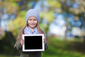 förtjusande liten flicka innehav läsplatta pc utomhus i höst solig dag foto