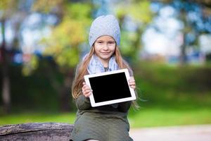 förtjusande liten flicka med läsplatta pc utomhus i höst solig dag foto