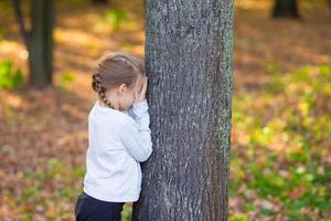 liten flicka spelar Dölj och söka nära de träd i höst parkera foto