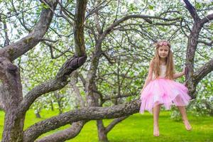 liten förtjusande flicka Sammanträde på blomstrande äpple träd foto