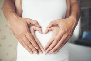 gravid kvinna och hennes man med händer som visar hjärtform foto