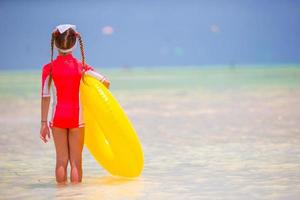 förtjusande liten flicka med uppblåsbar sudd cirkel under strand semester. unge har roligt på sommar aktiva semester foto