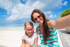 mor och liten flicka tar selfie på tropisk strand foto