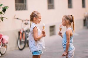 förtjusande liten flickor äter glass utomhus på sommar. foto