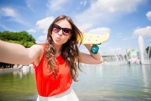 porträtt av Lycklig ung flicka tar selfie med skateboard utomhus foto