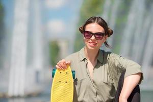 porträtt av Lycklig ung urban flicka med skateboard i europeisk stad. caucasian turist bakgrund de stor fontän foto