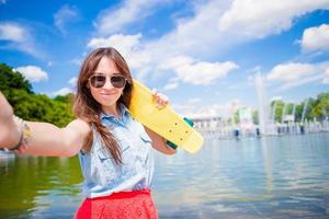 porträtt av Lycklig ung flicka tar selfie med skateboard utomhus foto