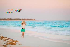 liten löpning flicka med flygande drake på tropisk strand. unge spela på hav Strand. foto