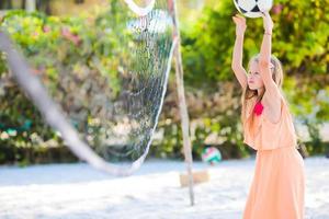 liten förtjusande flicka spelar volleyboll på strand med boll. sportig familj njut av strand spel utomhus foto