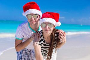 porträtt av unga par i santa hattar njuta av strandsemester foto
