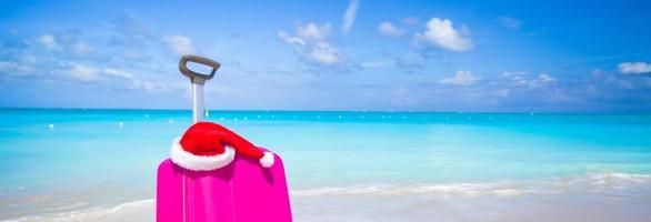 närbild av rosa resväska och santa claus hatt på strand foto