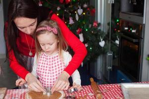 liten förtjusande flicka och ung mor bakning jul pepparkaka småkakor foto