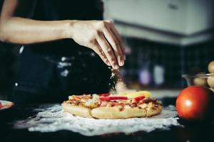 närbild av en hand som lägger oregano över en pizza