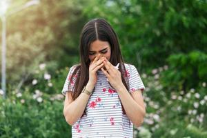 ung Söt kvinna nysning i främre av blomning träd. vår allergi begrepp. säsong- allergier och hälsa problem. sinus värk orsakar mycket målarfärgad huvudvärk. influensa kall symptom. sinus smärta foto